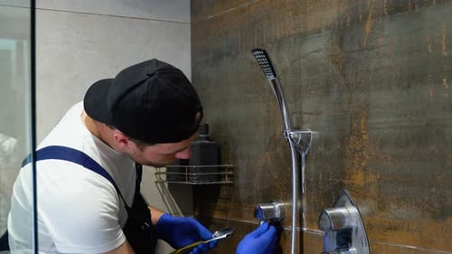 Joven fontanero con herramientas para reparar el grifo en la cabina de ducha