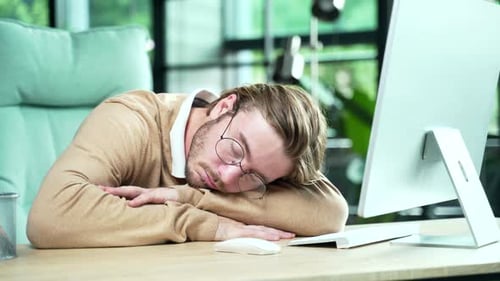 Exhausted overloaded young office worker with glasses sleeping dozing on workplace at working time
