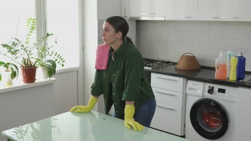 Woman Wearing Gloves Stands Thoughtfully in Kitchen