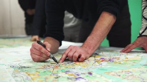 Ein vom Team umzingelter Mann verwendet einen Marker, um Notizen auf der Karte zu notieren