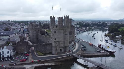 Ancient Caernarfon castle Welsh harbour town aerial view medieval waterfront landmark pull away orbi