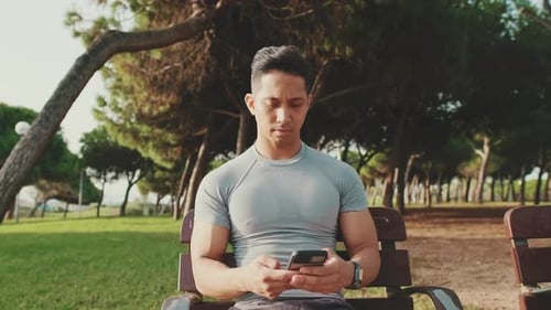 Young man sitting on a park bench uses a mobile phone