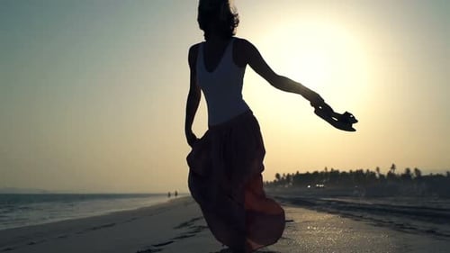 Silhouette einer jungen Frau, die bei Sonnenuntergang frei an einem schönen Strand tanzt
