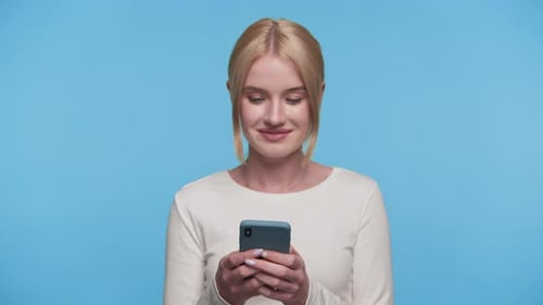 Woman Smiling While Texting on Smartphone on Blue Background