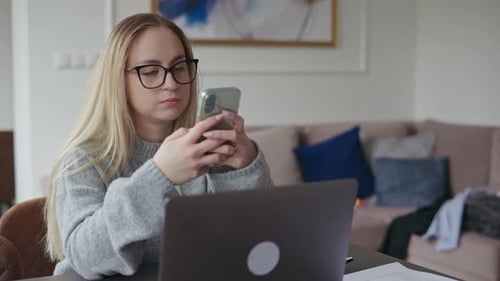 Woman Uses Mobile Phone While Working on Laptop