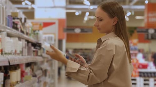 A Woman Wearing a Light Brown Shirt is in a Grocery Store Aisle She is Reaching for a Product and