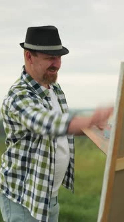 Painter in Hat and Checkered Shirt Creating Art in a Grass Field