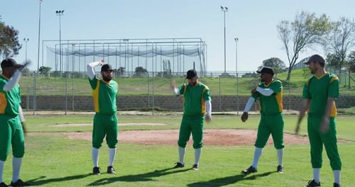 Diverse male teammates performing warm-up stretches on baseball field, with batting cage backdrop