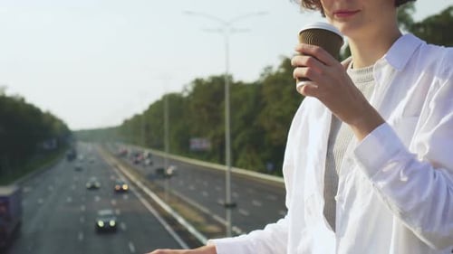 Woman Drinks Coffee Overlooking Busy Freeway