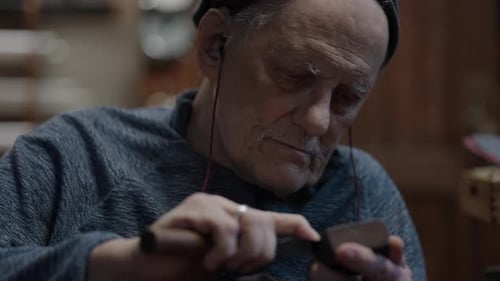 Senior Gray Haired Male Master in a Wheelchair Working at His Workshop Sharpening Japanese Deba