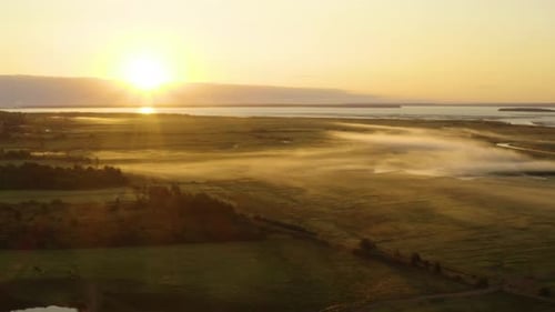 Scenic aerial view of the sun rising over the picturesque countryside on a misty, summer morning.