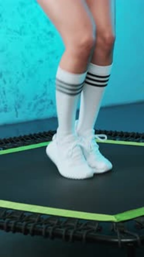 Close-up of legs of energetic young fitness girl in white sneakers jumping on mobile mini trampoline