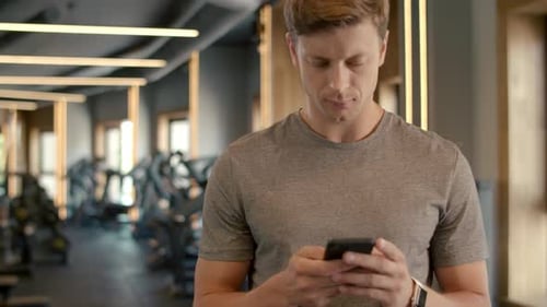 Handsome Sportsman Texting Message on Smartphone in Fitness Center. Closeup Serious Fitness