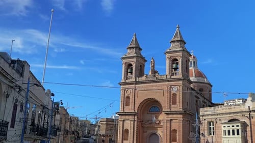 Historic Maltese church with twin bell towers and dome against a blue sky