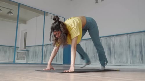 A woman performs a downward-facing dog pose on a yoga mat in a fitness studio.