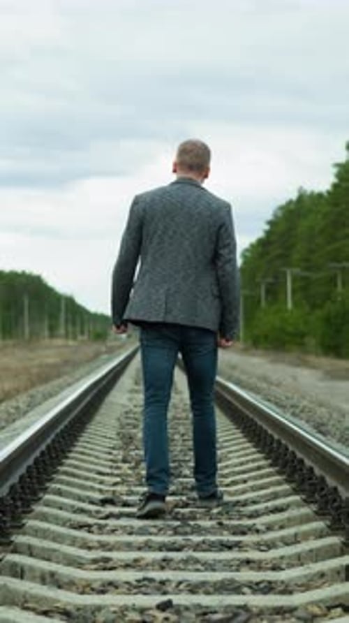 Man Walking Down Railroad Tracks on Overcast Day