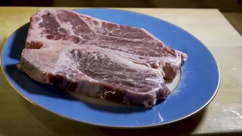 Große Platte rohen, ungekochten Steaks auf einem blauen Teller auf einem Holzschneidebrett. Slider von links nach rechts