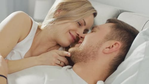 Glückliches junges Paar, das zusammen im Bett kuschelt, küsst und lächelt. Schöne blonde Frau und H