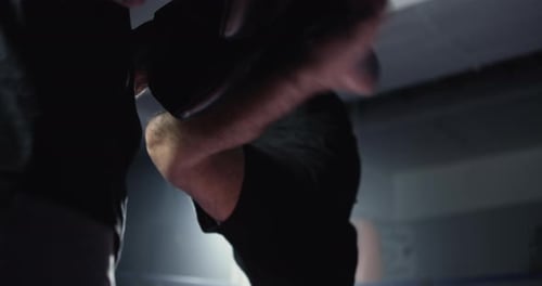 Fighters strikes a leg kick into cushioned pad during mitt training. Man kicking