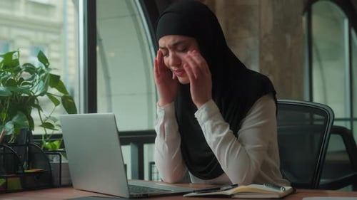 Woman in Hijab Massaging Temples at Office Desk