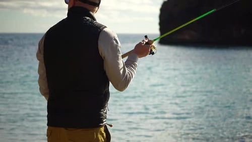 Man Hobby Fishing on Sea spannt eine Angelschnur, Fischrolle beruhigt die Oberfläche des Meeres bei sommerlichem Sonnenuntergang