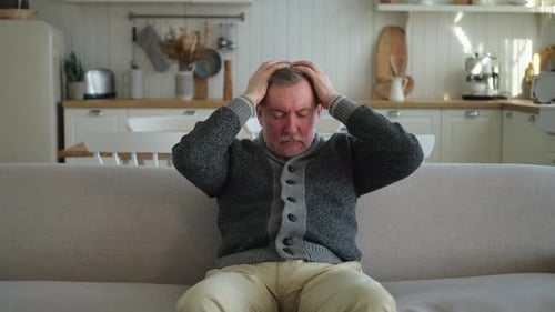 Man With Headache Sits on Couch