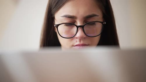 Nahaufnahme der Laptop-Hülle und der müden Augen einer jungen Frau mit Brille