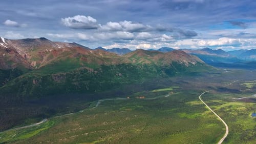 Die wellenförmige Straße überquert das riesige grüne Tal am Fuße der wunderschönen Berge.