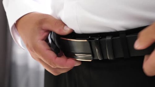 19. The man tightens the belt on his waist. Stylish men's accessories.