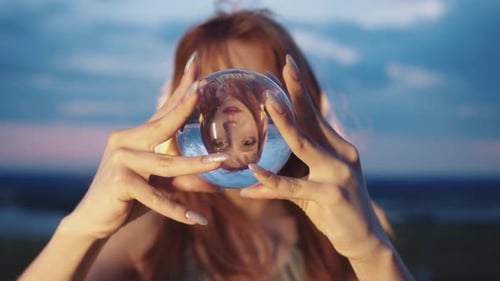 Woman Holds Glass Sphere Outdoors at Sunset