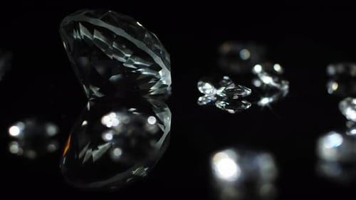 Slow turning large cristal clear diamond with smaller shiny diamonds on a dark mirroring surface to