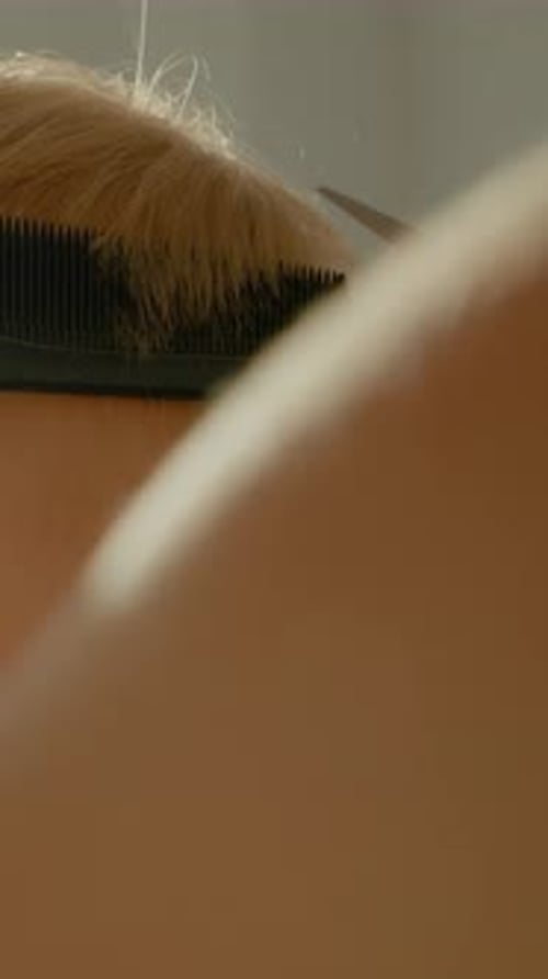 Vídeo vertical: La madre le corta el pelo a su hijo pequeño en casa con una cálida luz natural
