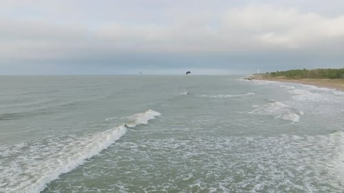 Establishing aerial view of a group of people engaged in kitesurfing, overcast winter day, high wave