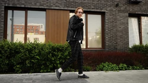 A Fashionable Guy Walks Down the Street Near a Residential Complex and Looks at the Camera A