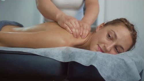 Relaxed Female Lying on Spa Bed with Happy Eyes is Relaxing During Back and Shoulder Massage Lying