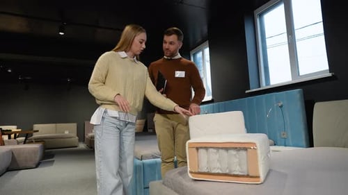 Woman Inspecting Mattress with Salesperson in Furniture Store