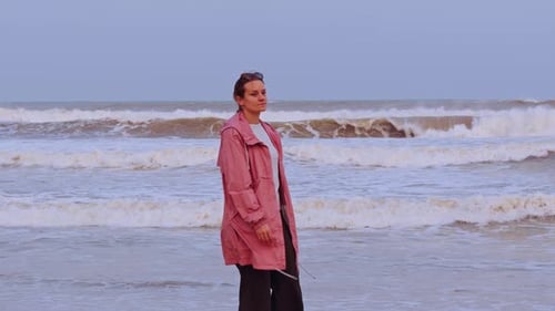 Low Angle Slow Motion View of a Woman in Pink Jacket Walking beside Foamy Shoreline with Strong Wave