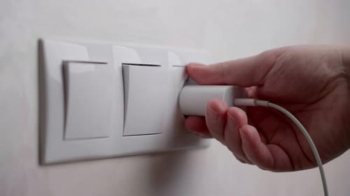 A man's hand takes out a smartphone charging plug from a socket