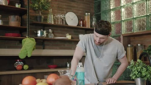 Young Man Listens to Music in Kitchen After Workout