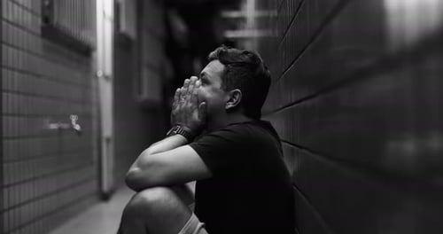 Man sitting in narrow alley with head in hands, deep emotional struggle, solitude, mental health