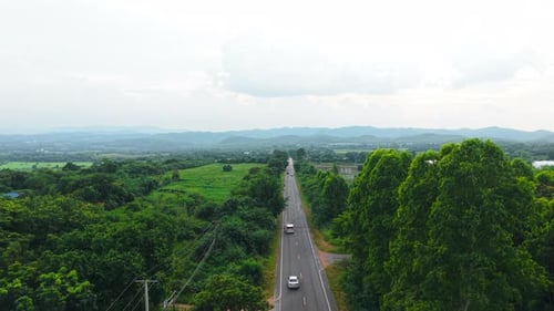 Vehicles Traveling on a Long Straight Paved Road That Crosses a Wide Valley Surrounded By Lush