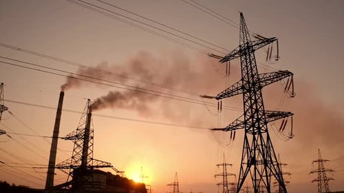 Electricity pylons against smoke stacks at sunset. High-voltage electric towers on the evening sky.