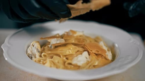Closeup in a Professional Kitchen Chef in Black Gloves Put Dry Bread Over Pasta