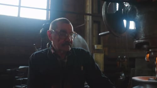Labourer with Spectacles Sits By Drilling Machine at Factory