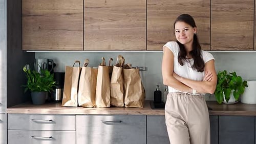 Young Woman Next to Paper Bags Full of Food in Kitchen Groceries Ordered Online and Delivered By