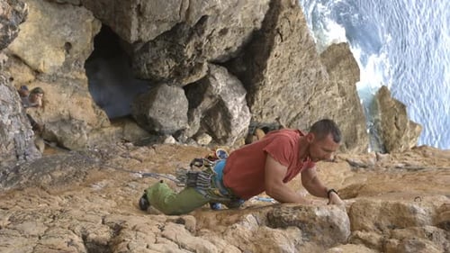 A Man is Climbing a Rock Wall with a Rope Around His Waist