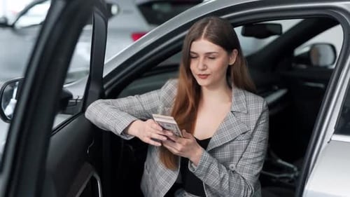 Stylish young woman scattering dollar bills while sitting in the car