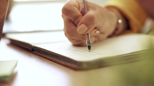 Woman, hand and pen writing in a notebook at home working on study schedule and learning plan