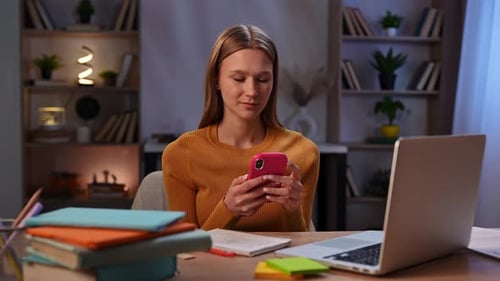 Young Woman Using Smartphone While Working at Home Office Desk
