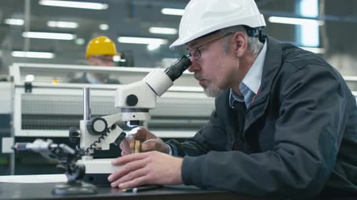 Un ingénieur principal inspecte un détail au microscope dans une usine.
